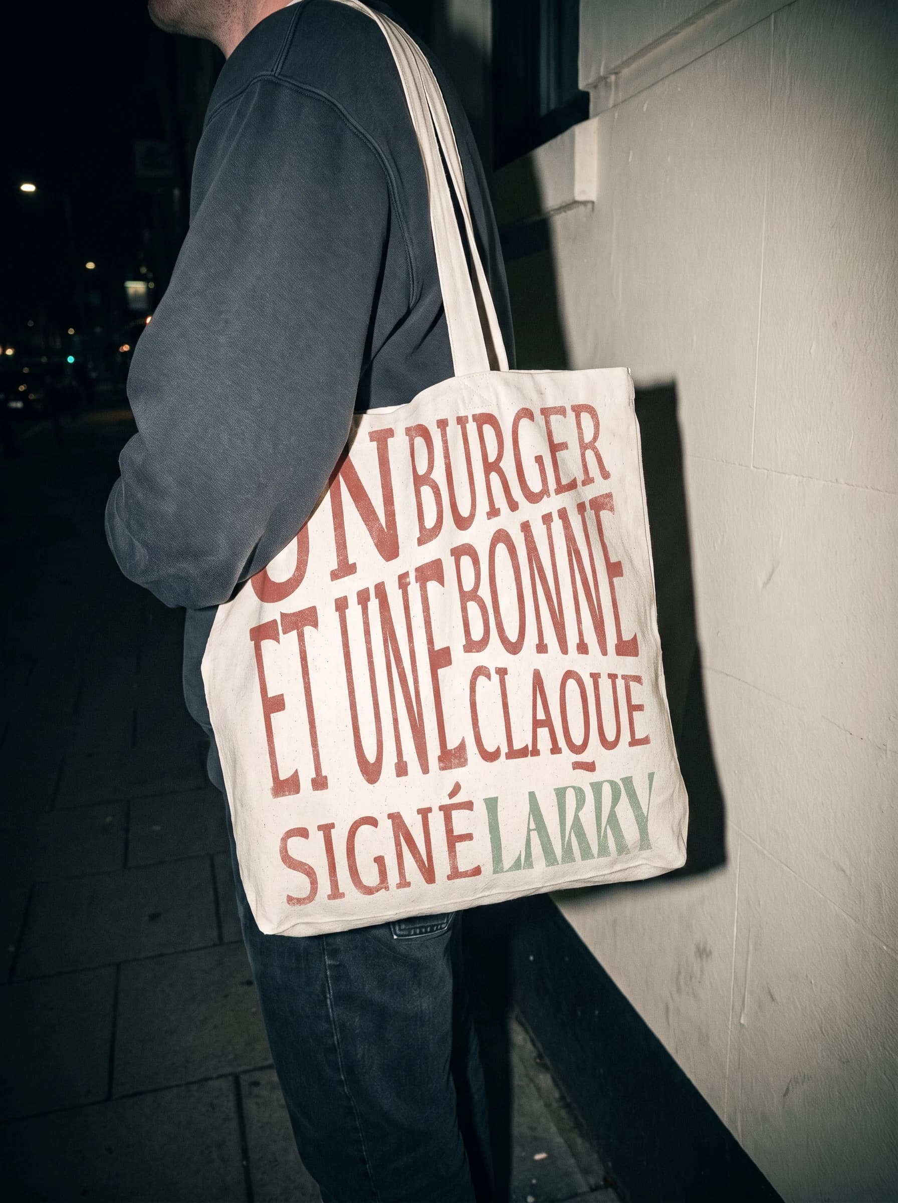 Tote bag canvas porté au flanc, slogan Un burger et une bonne claque signé Larry, flash de nuit